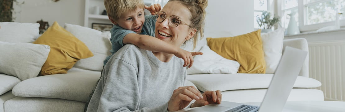 Boy pointing at laptop while standing behind mother at home